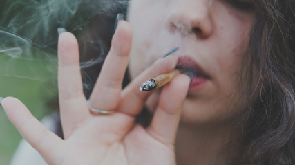 Obraz premium Girl smoking medical marijuana joint outdoors, close-up. Cannabis is a concept of herbal medicine.