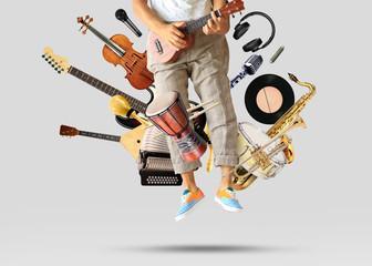 Young man sits and plays guitar among musical instruments