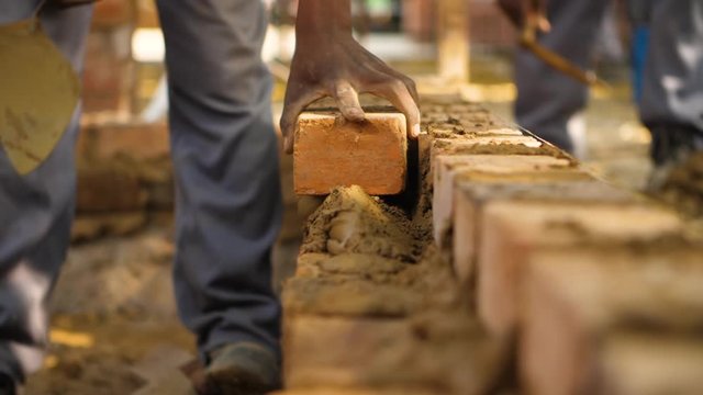Linear shot of blue collar worker laying bricks in slow motion.