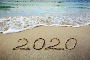 Year 2020 written at the caribbean sand beach with sea wave .