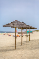 View of a beach with four straw parasol, summer weather with tourist people taking sunbathing