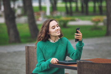 Young beautiful adult girl with natural makeup fashionable and happy with tablet and mobile in summer cafe