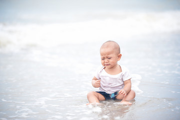 Asian ten month baby girl sitting and crying on the beach, worrying mother will leave her alone. Baby worries playing the beach first time.