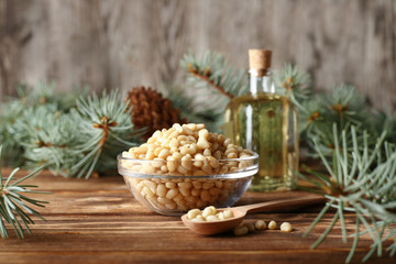 Cedar pine nuts in glass bowl with cones, oil, spoon, cedar brunch on wooden background.