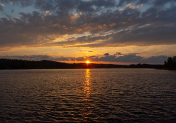 Amazing sunset in Finland during summer evening. Golden hour and dramatic clouds. Reflection in water, calm scenery.