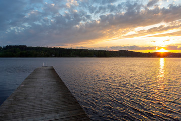 Long wooden pier during sunset in Finland. The dock on the left side, sun going down on the right. Copy space.