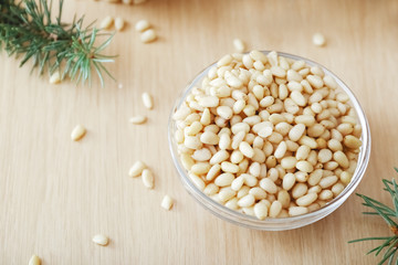 Cedar pine nuts in glass bowl with cedar brunches on wooden background.