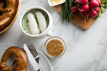 Münchener Weißwurst in Terrine mit bayrischer süßen Senf, Brezel, Radieschen, Schnittlauch und Butter auf Marmor Tisch