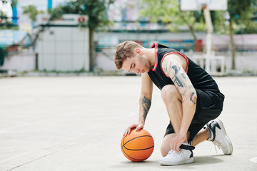 Serious young fit sportsman tying shoes before basketball game