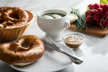 Münchener Weißwurst in Terrine mit bayrischer süßen Senf, Brezel, Radieschen, Schnittlauch und Butter auf Marmor Tisch
