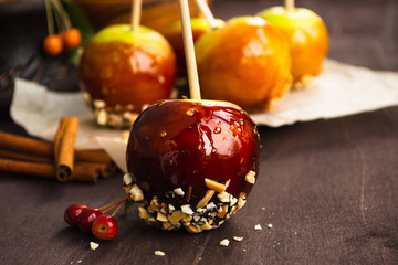 Homemade caramel apples on a stick. Green apples in caramel sauce and nuts decorated for Halloween. Classic autumn dessert. Rustic style.