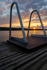 Sunset behind the ladder on the pier end. Lake view with golden hour and dramatic sky.