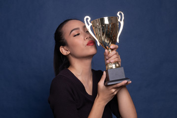 Back view of successful young asian woman holding a trophy.