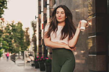 Beautiful smiling woman drink coffee walking on the city in summer day.