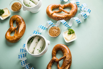 Münchener Weißwurst in Terrine mit bayrischer süßen Senf, Brezel und Butter mit Oktoberfest Luftschlangen auf Pastell grünen Hintergrund