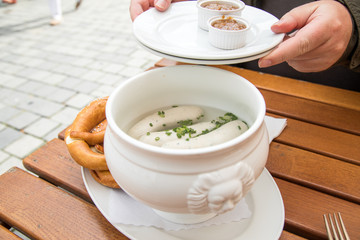 Mann isst Münchener Weißwurst mit Messer und Gabel, süßen Senf und Brezel und löst Wurst richtig aus Pelle draußen in Biergraten