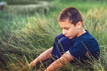 A child with Down syndrome and cerebral palsy is sitting in the grass. Loneliness of a sick person.