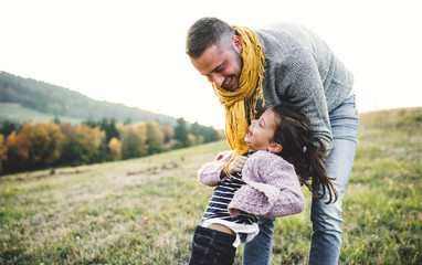 A rear view of young father having fun with a small daughter in autumn nature.