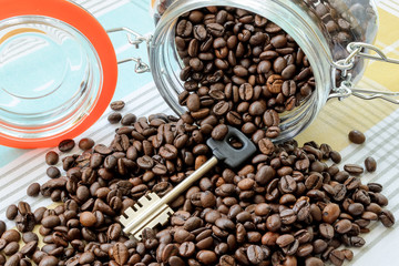 Large key and coffee beans was scattered from fallen glass jar on a tablecloth. Can for bulk food products as a cache or safe. To hide something. Key in a jar concept.
