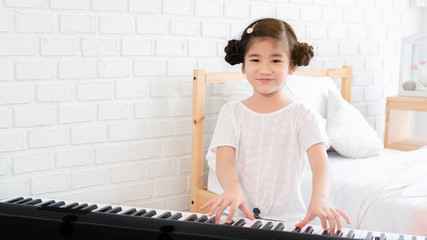 Fototapeta na wymiar Asian girl is doing an activity to learn to play electric piano. In the white bedroom Practicing music will give you good emotional skills, relax, good mental health and good mood. copy space