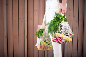 Girl holding mesh shopping bag and cotton shopper with vegetables without plastic bags, wooden...