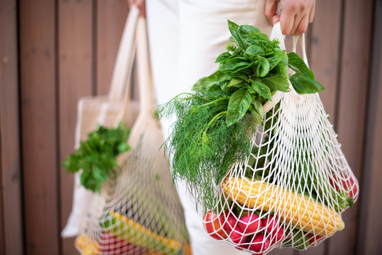 Zero waste concept with copy space. Woman holding cotton shopper and reusable mesh shopping bags with vegetables, products. Eco friendly mesh shopper. Zero waste, plastic free concept.
