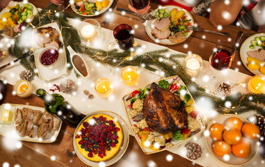 christmas dinner and eating concept - roast chicken or turkey and other food on table over snow
