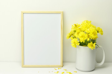 Frame mockup with yellow flowers in clear glass with water on white background and copy space.