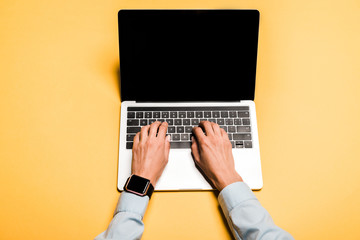 cropped view of woman typing on modern laptop with blank screen on orange