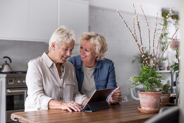 Mature lesbian couple looking at digital tablet together at home