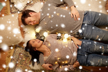 christmas, hygge and people concept - happy couple with garland lying on floor at home over snow
