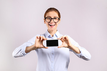 Young beautiful woman in formalwear with slim body posing over grey isolated background, copy space for text. Portrait of attractive female with hair tied in ponytail wearing glasses & blue blouse.