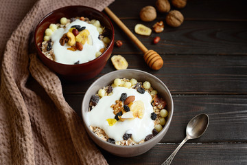 Granola with yougurt, nuts, dried fruits on wooden brown background