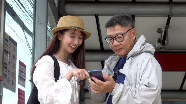 Asian young lady and father's tourist is standing, looking at the map in an application on a smartphone while traveling around Bangkok.