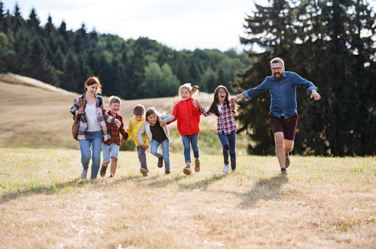 Group of school children with teacher on field trip in nature, running.