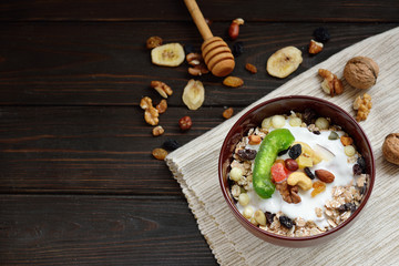 Granola with yougurt, nuts, dried fruits on wooden brown background