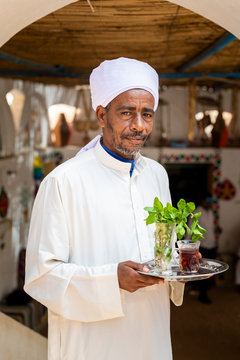 An Egyptian man holds a tray with a glass of mint tea and some fresh mint leaves, Aswan, Egypt