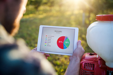 A midsection of farmer with tablet standing outdoors in orchard.