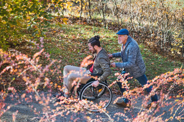 Senior father and his son in wheelchair on walk in nature.