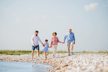 Multigeneration family on a holiday walking by the lake, holding hands.
