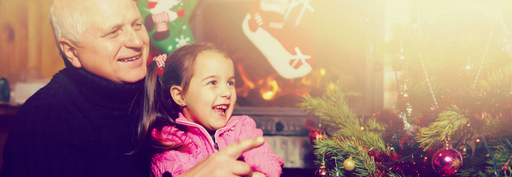 Grandfather and granddaughter sitting on floor and looking at digital tablet during christmas. Man with his little girl having a video on digital tablet.