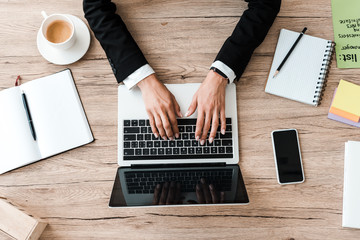 top view of businesswoman typing on laptop near cup of coffee in office