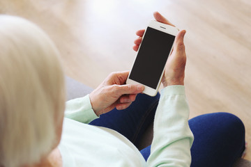 Elderly woman holding blank screen cell phone gadget in hands. Old lady with wrinkled skin trying to vigure out touchscreen smartphone. Background, close up, overhead, top view, copy space.