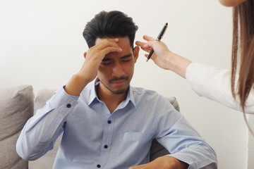 Asian professional female psychiatrist giving advice to a stressed man having headache and migraine problem due to his health problem both physical and mental disorder. Needs remedy and more resting