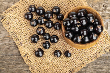 Black currants in bowl on burlap and wooden background.Top view. Flat lay pattern