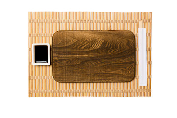 Empty rectangular brown wooden plate with chopsticks for sushi and soy sauce on yellow bamboo mat background. Top view with copy space for you design