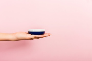 Female hand holding cream bottle of lotion isolated. Girl give jar cosmetic products on pink background