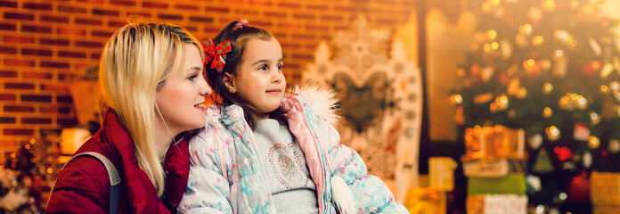 Happy family mother and little daughter sitting beside the decorated Christmas tree and gift boxes