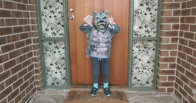 young boy dressed in a werewolf costume for Halloween raises his hands like claws to look scary but in reality looks very cute