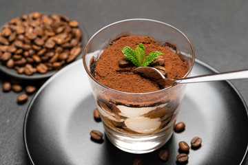 Portion of Classic tiramisu dessert in a glass cup on dark concrete background